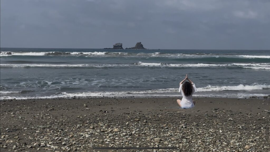 Tanya LeRose meditating on a beach with the Pacific ocean behind her